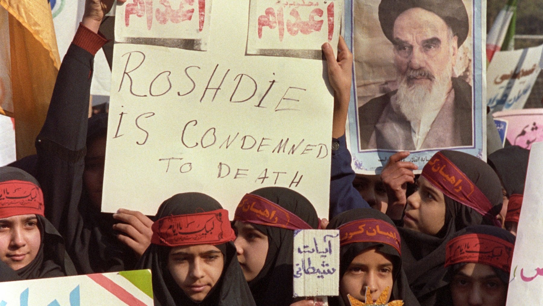 Ragazze protestano a Tehran chiedendo la morte dello scrittore indiano britannico Salman Rushdie dopo la fatwa scagliata contro di lui dall'Ayatollah Ruhollah Khomeini, 1989. Uno dei cartelli riporta in maniera errata il nome di Rushdie. (c) Kaveh Kazemi/ Getty Images&nbsp;
