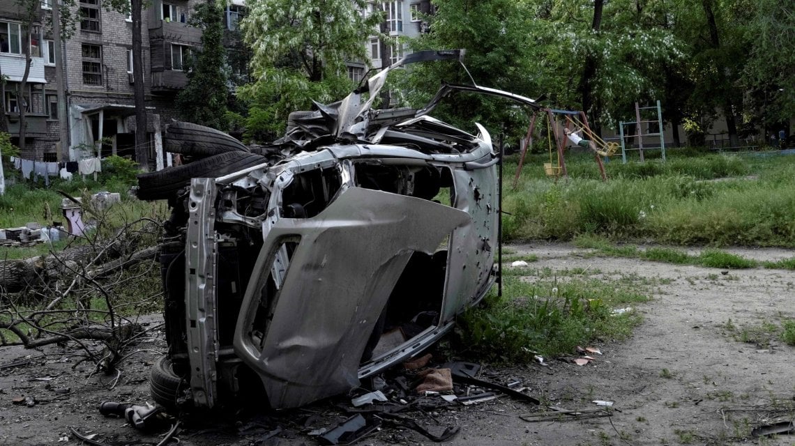 A boy plays on a swing near a destroyed car in a residential area of Mariupol on May 29, 2022, amid the ongoing Russian military action in Ukraine