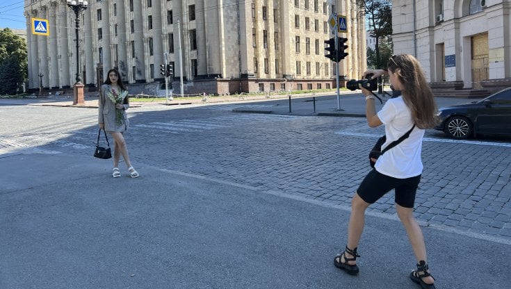 Le due amiche. Katia Striliana fotografa l&rsquo;amica Anna Nikulina, con un mazzetto di fiori in mano, davanti al palazzo del Comune bombardato. Prima dell&rsquo;invasione russa Katia, 22 anni, era studentessa alle magistrali e Anna, 23, agente di turismo. Brunella Giovara 