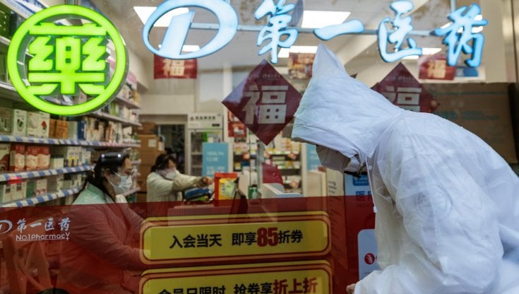Un uomo con mascherina e tuta protettiva passa davanti a una farmacia a Shanghai (Epa/Alex Plavevski)