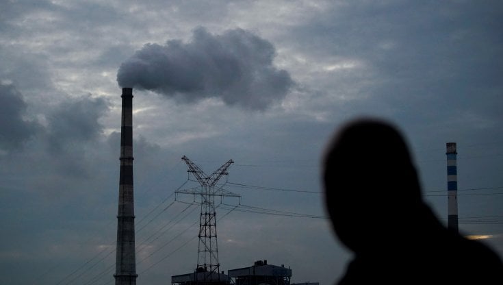 Un uomo cammina vicino a una centrale alimentata a carbone a Shanghai, Cina