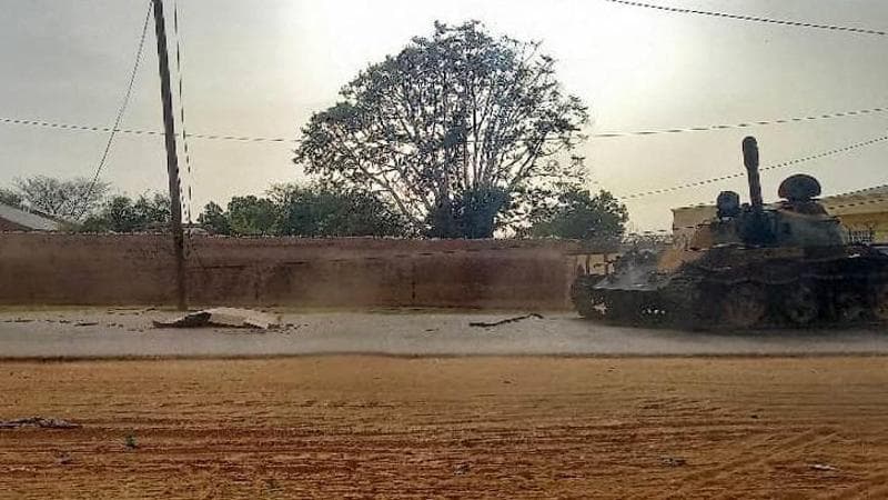 Un cadavere ricoperto con dei cartoni davanti a un veciolo militare nelle strade di El Geneina
