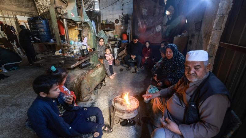 TOPSHOT - Members of a Palestinian family who fled Gaza City to Khan Yunis and had to recently flee to Rafah in the southern Gaza Strip, gather around a small fire, inside a workshop where they found temporary shelter, on December 9, 2023, amid continuing battles between Israel and the militant group Hamas. Israel pressed its offensive against Hamas militants in Gaza on December 9, after the United States blocked an extraordinary UN bid to call for a ceasefire in the two-month war. (Photo by MOHAMMED ABED / AFP)