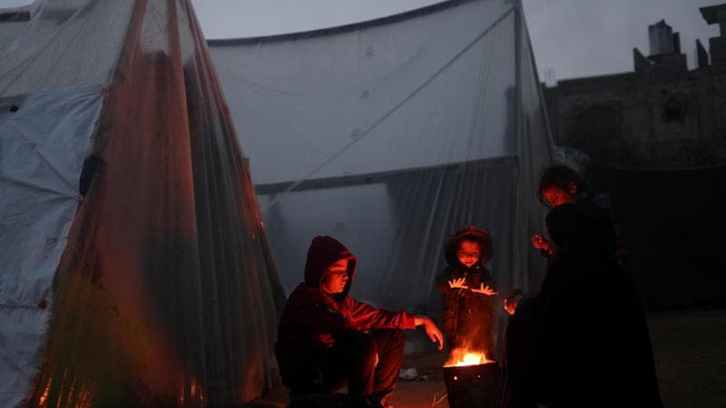 Rifugiati cercano di scaldarsi in una tendopoli a Rafah