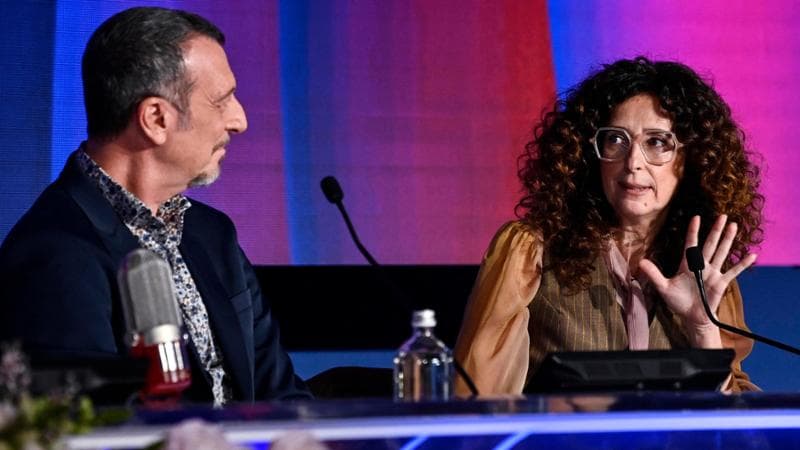 Conferenza stampa, Amadeus sbotta su John Travolta: “Creato un caso che non c’è”. E la Rai: “Nessuna pubblicità occulta alle scarpe ma è stato fatto un errore”
