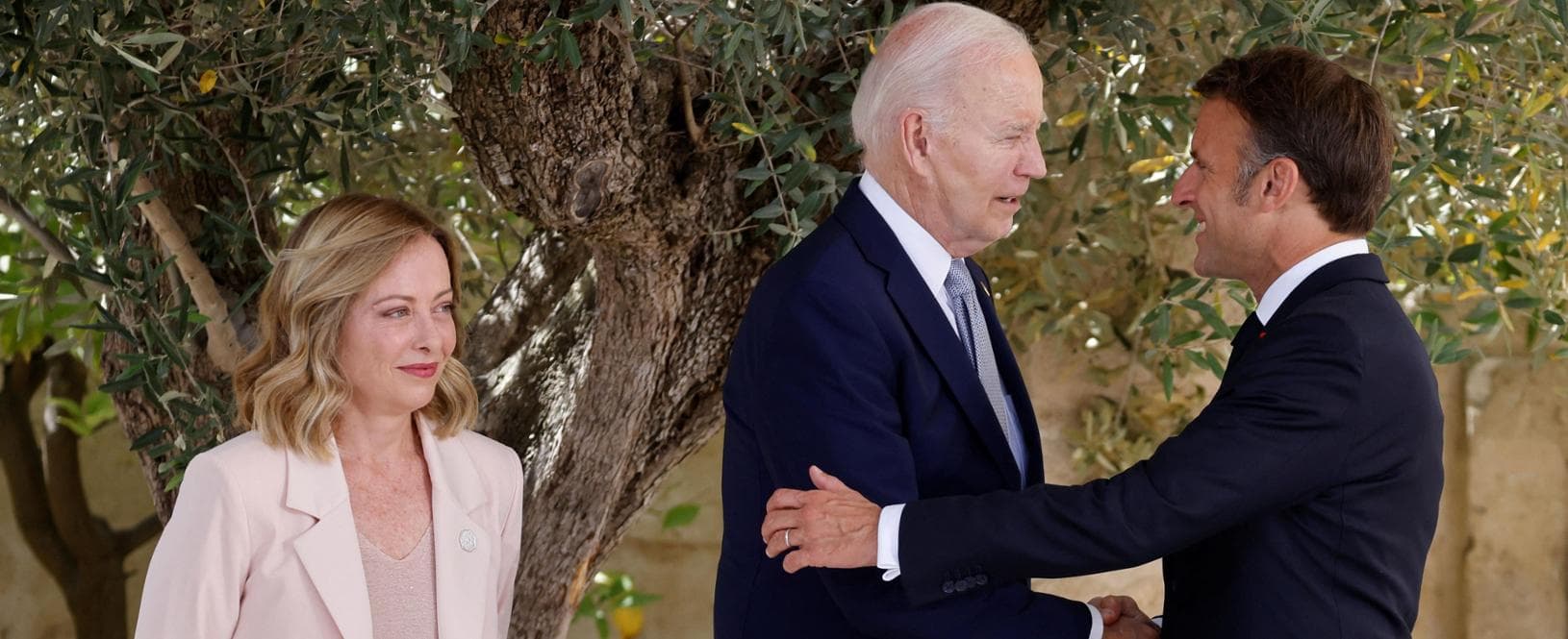 French President Emmanuel Macron (R) shakes hands with US President Joe Biden (C) as Italy's Prime Minister Giorgia Meloni looks on, upon arrival at the Borgo Egnazia resort for the G7 Summit hosted by Italy in Apulia region, on June 13, 2024 in Savelletri. Leaders of the G7 wealthy nations gather in southern Italy this week against the backdrop of global and political turmoil, with boosting support for Ukraine top of the agenda. (Photo by Ludovic MARIN / AFP)