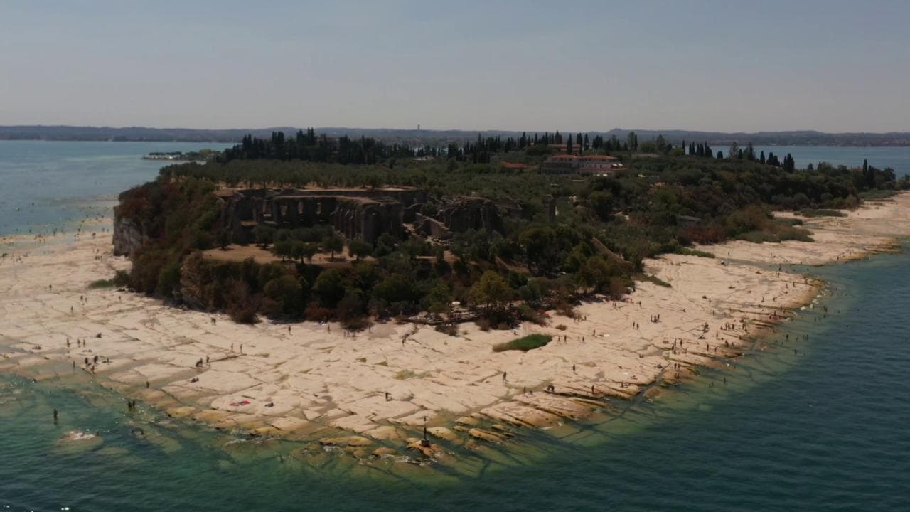 Lago di Garda, livello bassissimo delle acque per siccità: a Sirmione spunta una spiaggia di roccia