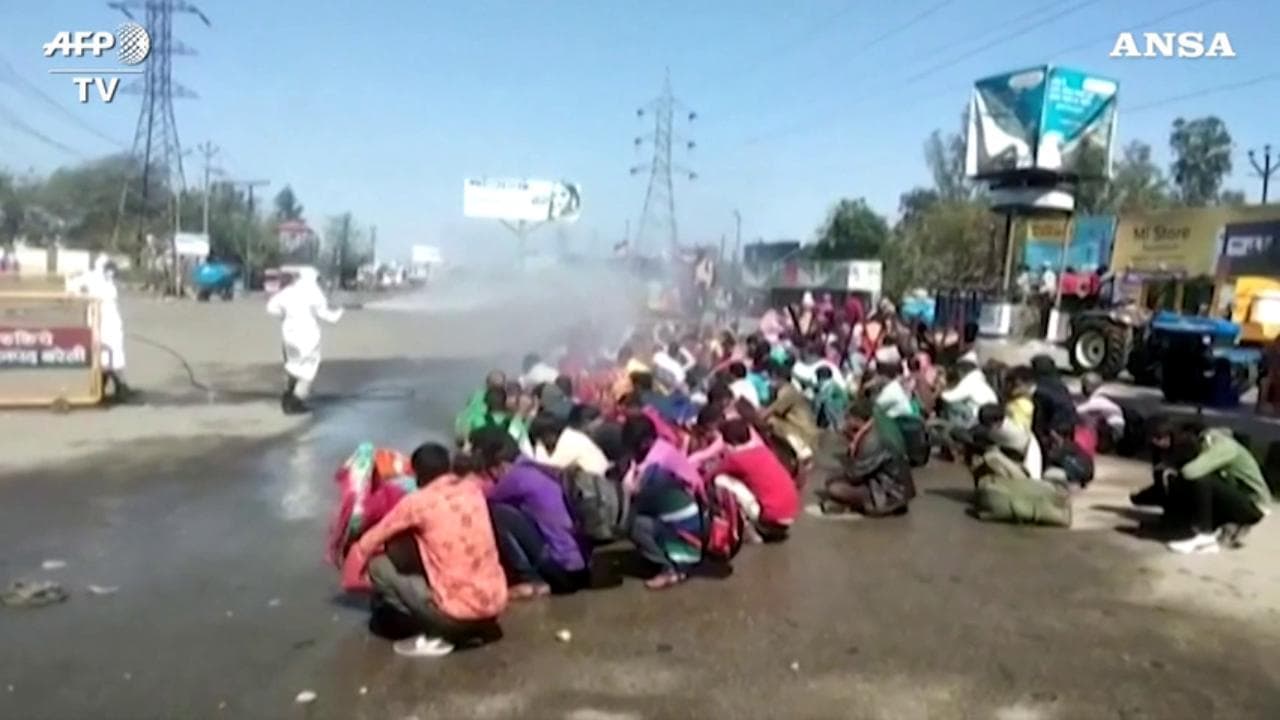 Coronavirus, accorpati in strada e bagnati con una pompa: così in India vengono disinfettati i migranti