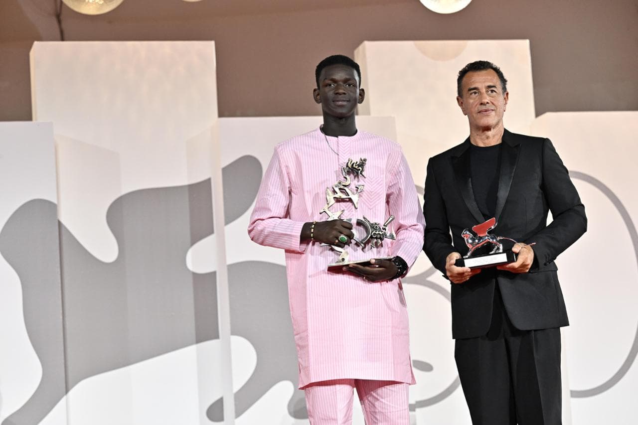 Seydou Sarr con il premio "Marcello Mastroianni" come miglior attor esordiente, insieme al regista Matteo Garrone alla Mostra di Venezia 2023