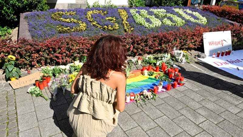 Una donna lascia dei fiori vicino al luogo dell'attacco a Solingen. Per terra alcuni cartelli con la scritta "Warum", perch&eacute; in tedesco
