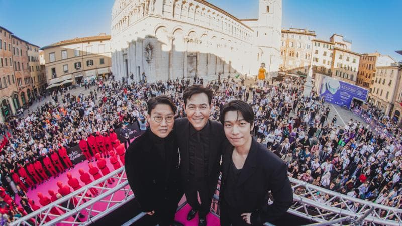 Folla a Piazza San Michele a Lucca per il lancio mondiale di Squid Game 2, dal 26 dicembre su Netflix. Da sinistra, l’autore Hwang Dong-hyuk e gli attori Lee Jung-jae 
e Wi Ha-jun. Virginia Bettoja, Netflix