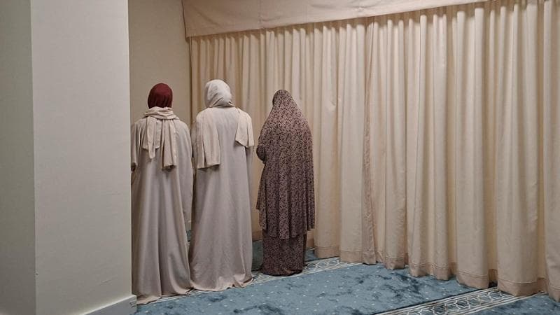 Tre studentesse, dopo avere indossato l’abaya, recitano la preghiera islamica delle 17 in una sala dell’università Magna Graecia di Catanzaro: la tenda bianca le separa dai fedeli uomini. (Chiara Spagnolo)