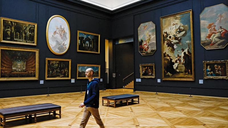 A staff member walks past 18th century Italian paintings hung in the newly renovated "Salle Piazzetta" housed in the "Aile Denon" (Denon wing) of the Louvre museum, ahead of its reopening to the public, in Paris, on December 2, 2025. (Photo by Ian LANGSDON / AFP)