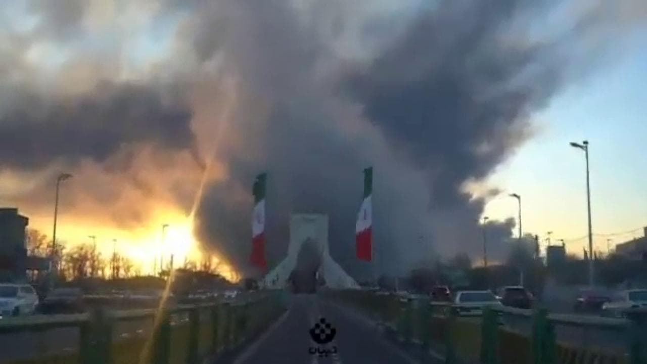 Teheran, la Torre Azadi simbolo della città nel fumo del raid: auto e bus carbonizzati sulla strada