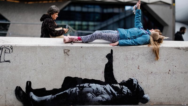 Londra, una bambina in posa accanto a un'opera di Banksy