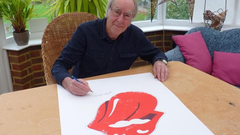 Pasche in una foto recente mentre firma un poster con la famosa lingua scelta come logo dalla band inglese