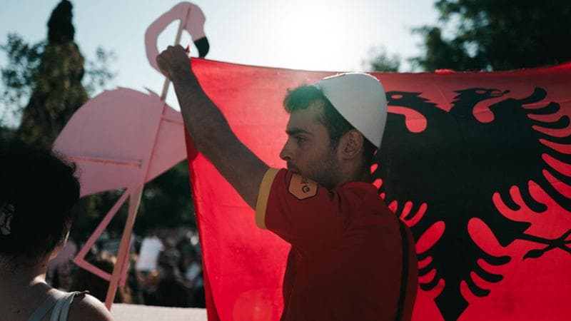 (Un giovane con la bandiera albanese e la sagoma degli animali dell’isola di Sazan)
