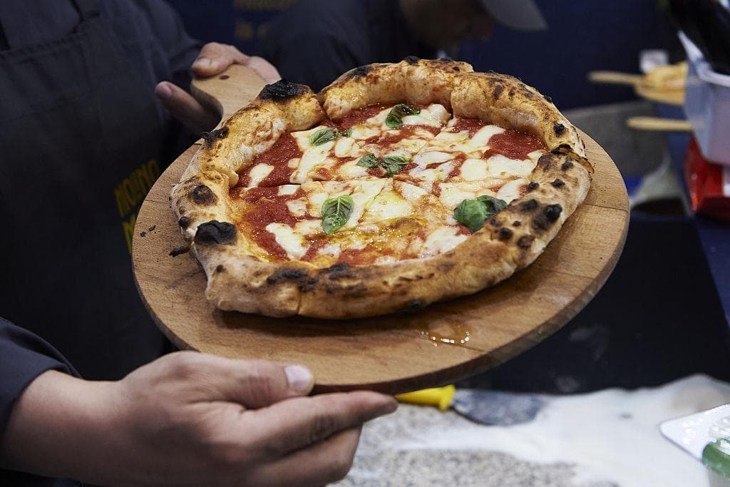 A pizza maker shows off a pizza in Naples