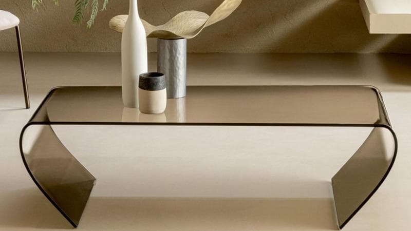 Linee morbide ed essenziali e sfumature calde per il tavolino Break di Riflessi, realizzato in cristallo curvato trasparente bronzato. Design di Riflessi Lab
